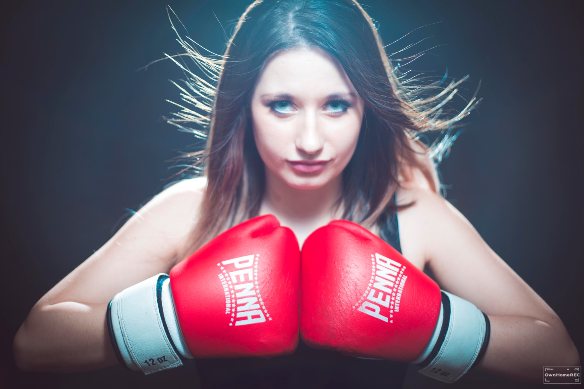 Portret kobiety w czerwonych rękawicach bokserskich Penna 12 oz na ciemnym tle, z rozwichrzonymi włosami i intensywnym spojrzeniem, wykonany w Warszawie.