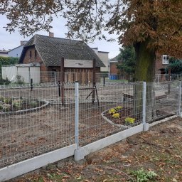 Ogrody z duszą Nie przesadzaj S.C - Nowo zamontowane, metalowe ogrodzenie panelowe z podmurówką betonową, otaczające teren z rabatami kwiatowymi i drzewami, w tle budynki mieszkalne.