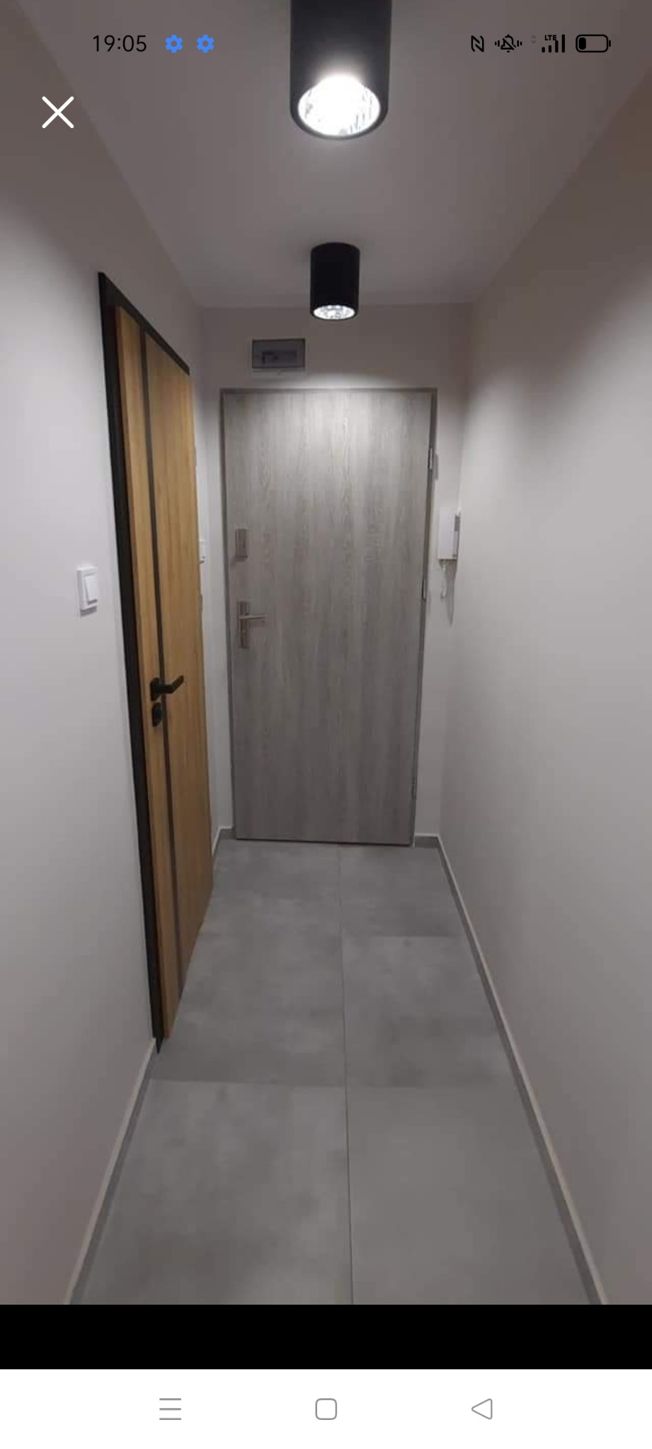 Korytarz w mieszkaniu po remoncie, widoczne dwie pary drzwi, szare płytki podłogowe i dwa nowoczesne, czarne reflektory sufitowe.