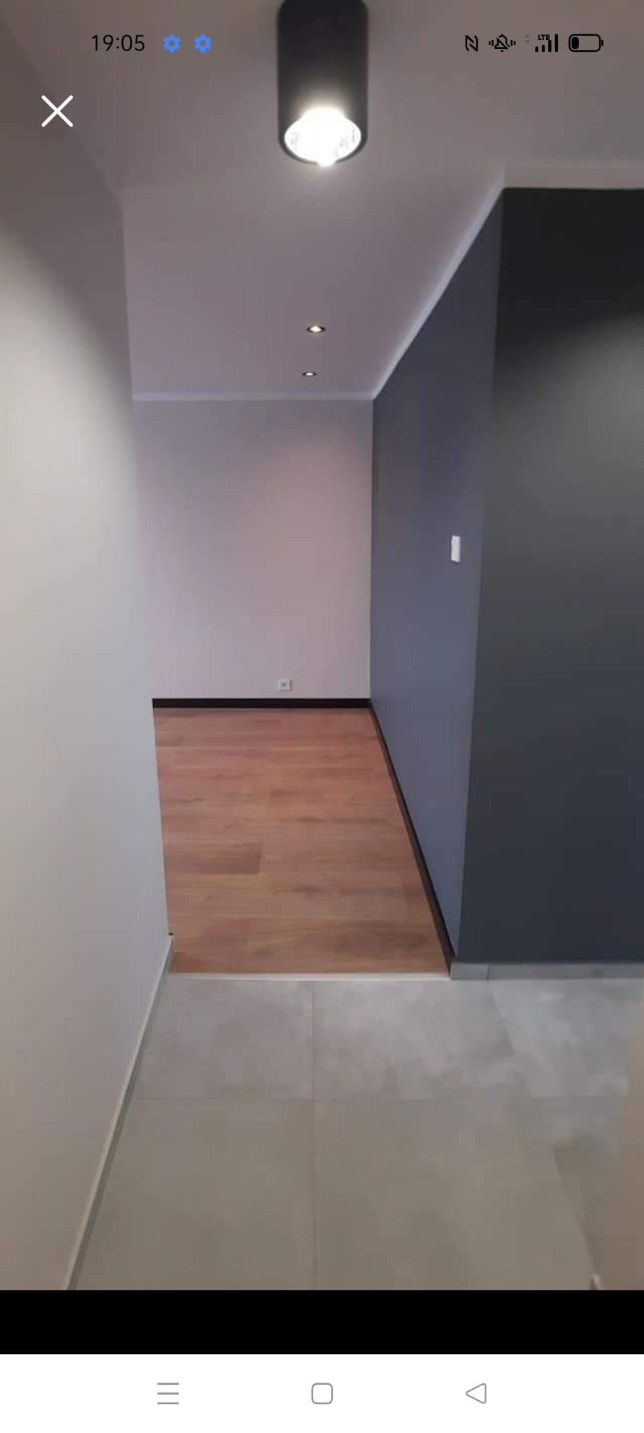 Wnętrze po remoncie: połączenie szarej ściany, jasnych ścian i podłogi z paneli w odcieniach drewna, widoczne także płytki podłogowe i oświetlenie sufitowe.