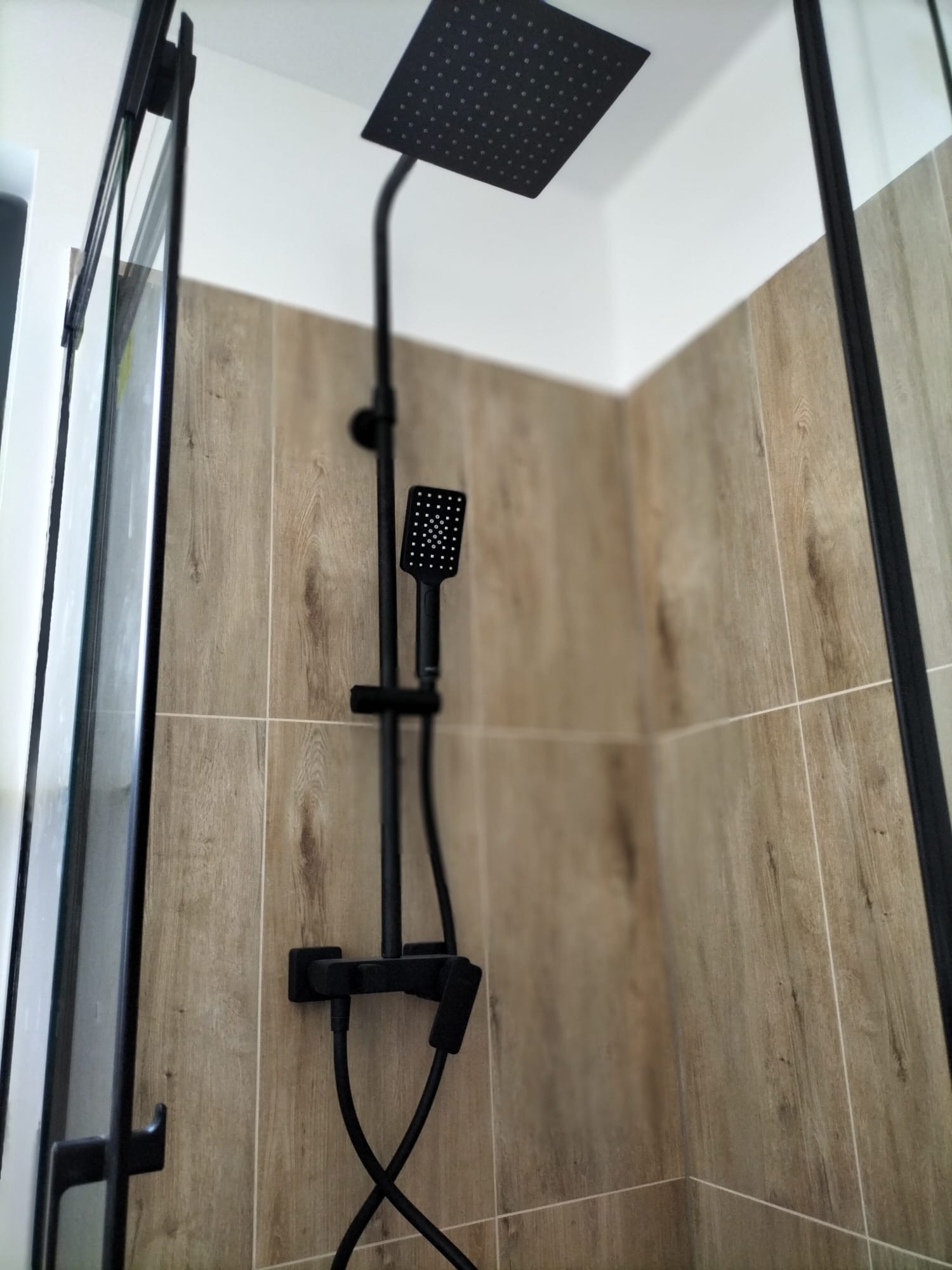 Nowoczesna kabina prysznicowa z czarną armaturą, płytki imitujące drewno, widok z dołu na deszczownicę i słuchawkę prysznicową.