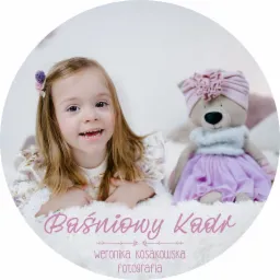 Uśmiechnięta dziewczynka z blond włosami i fioletową spinką, leżąca na puszystym białym tle obok pluszowego misia w turbanie i tiulowej spódniczce, ujęcie w okrągłej ramie.