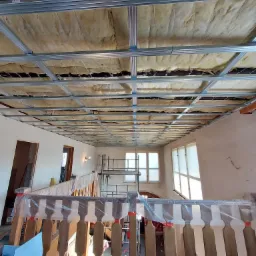 Montaż sufitu podwieszanego z izolacją z wełny mineralnej w Mikowicach, widok z dołu na metalową konstrukcję i ocieplenie przed zakryciem płytami gipsowo-kartonowymi.