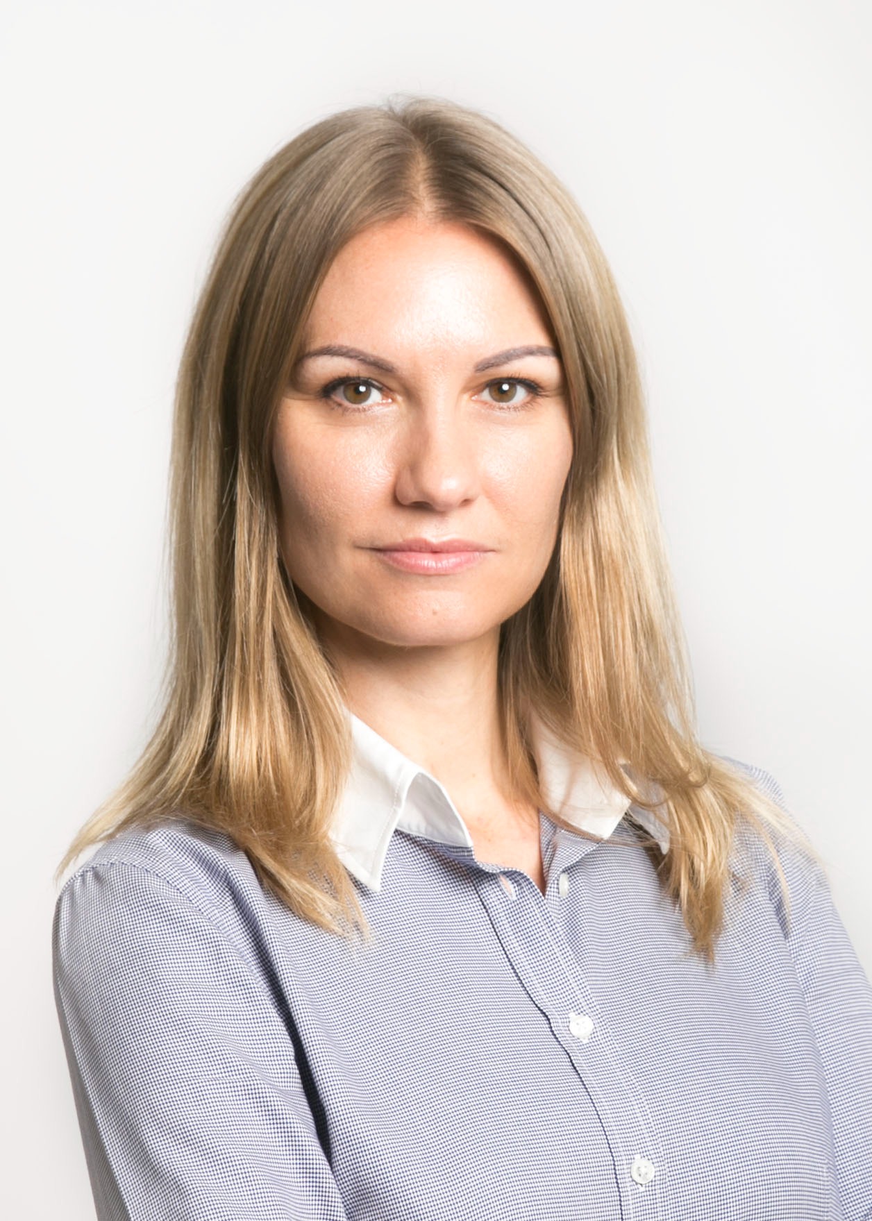 Portret kobiety z blond włosami, ubranej w niebieską koszulę z białym kołnierzykiem, na jasnym tle.