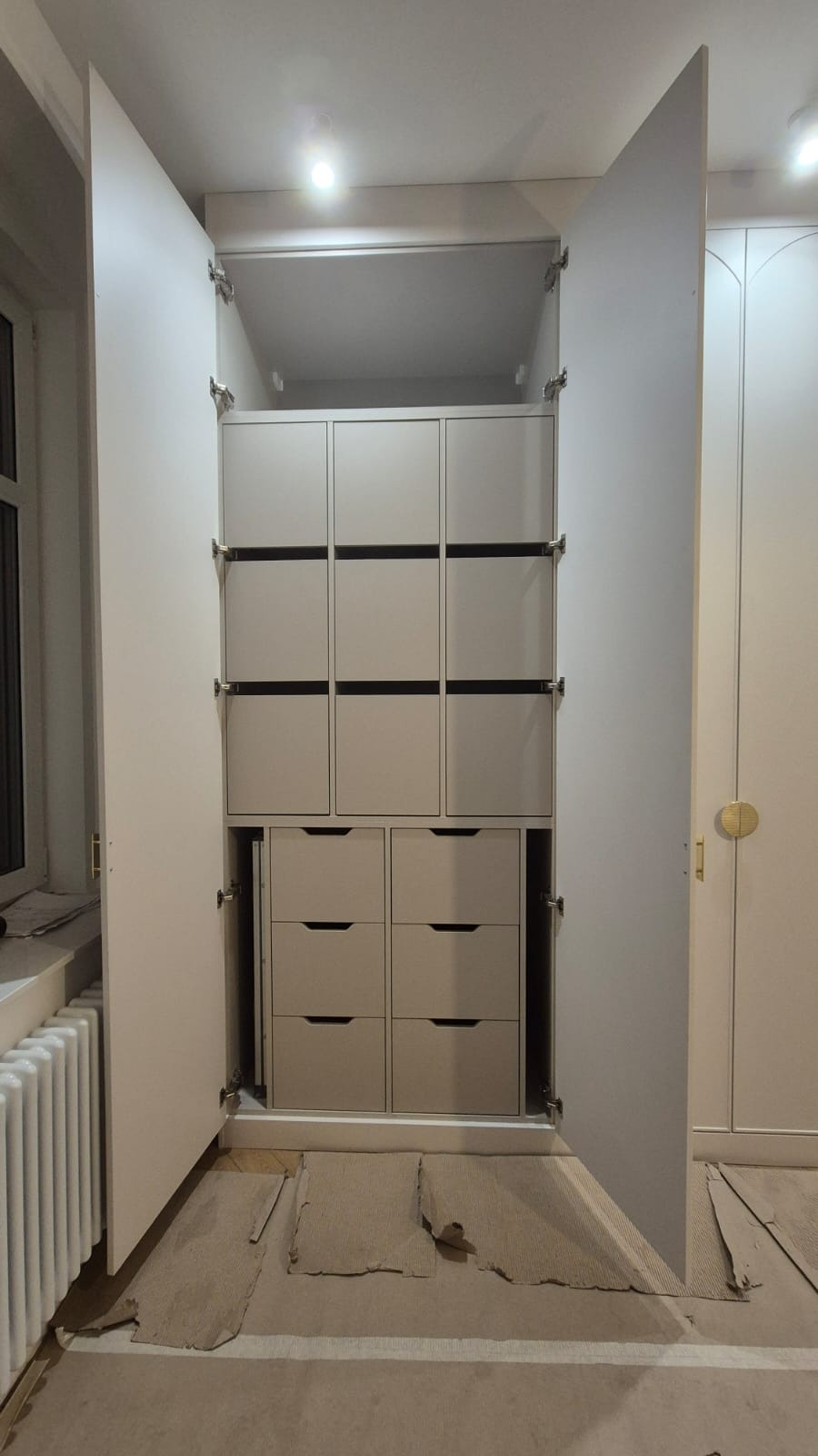 Wnętrze szafy na wymiar z szufladami i półkami, widoczne otwarte drzwi i zabezpieczenia podłogi kartonem.