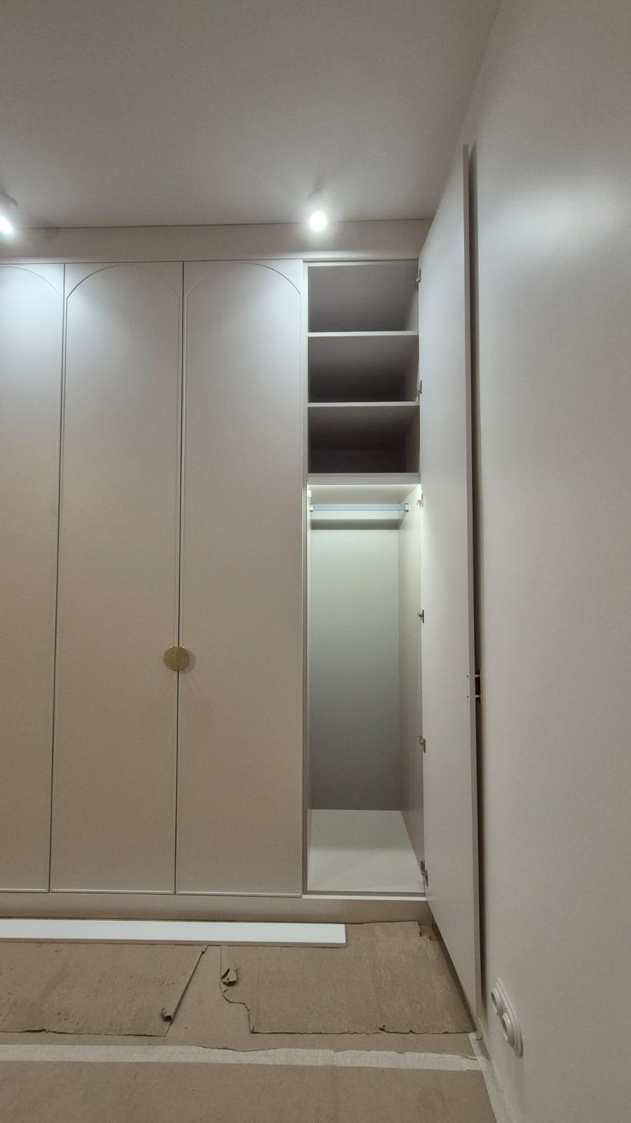 Jasna, minimalistyczna szafa na wymiar z otwartymi drzwiami, ukazująca półki i drążek na ubrania, wykonana w Opolu, widoczny fragment zabezpieczonej podłogi.