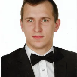 Portret młodego mężczyzny w czarnym garniturze i muszce na białym tle.