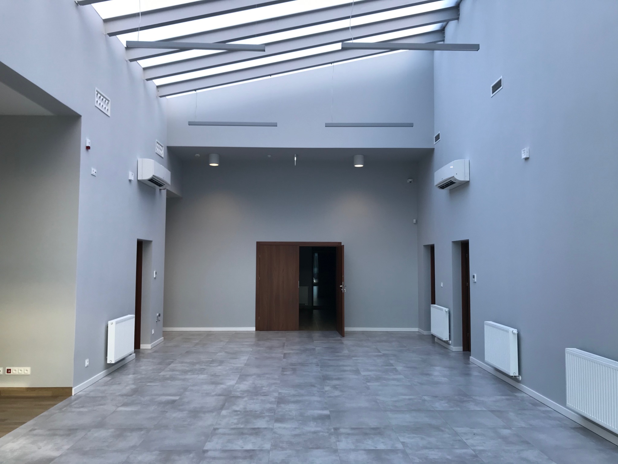 Przestronne, odnowione wnętrze biurowe z szarą podłogą z płytek, grzejnikami, klimatyzatorami i oknami dachowymi, świeżo po remoncie.