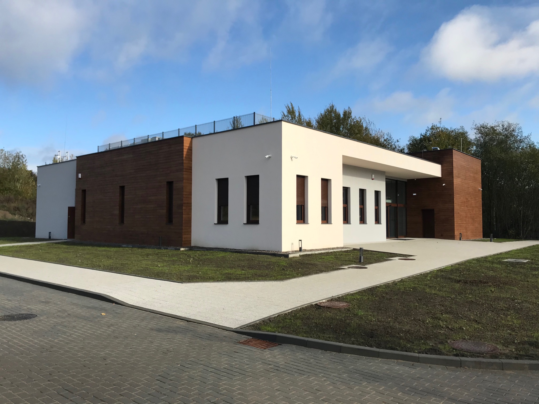 Nowoczesny budynek biurowy z elementami drewnianymi i białymi, minimalistyczna architektura, widok z zewnątrz, świeżo zagospodarowany teren.