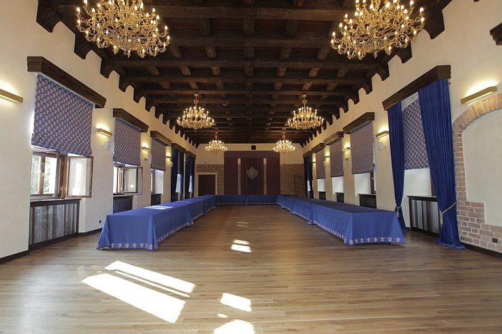 Sala balowa z drewnianym sufitem, kryształowymi żyrandolami i stołami nakrytymi niebieskimi obrusami, przygotowana na uroczystość.