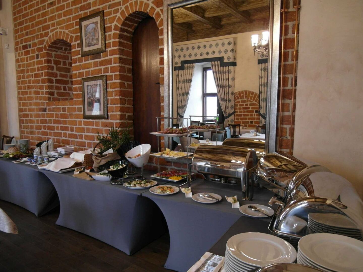 Stół szwedzki z cateringiem na tle ceglanej ściany i lustra odbijającego salę balową.