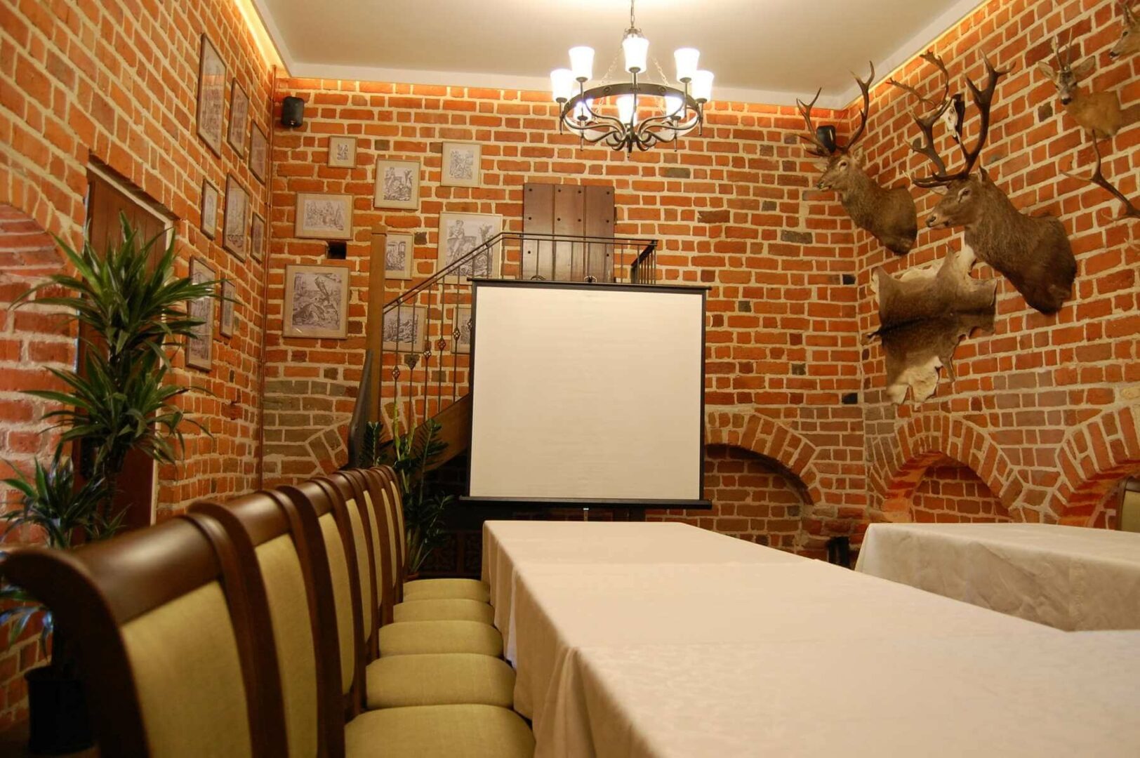 Sala konferencyjna z ceglanymi ścianami, dekorowana trofeami myśliwskimi, przygotowana do prezentacji z projektorem i ekranem.