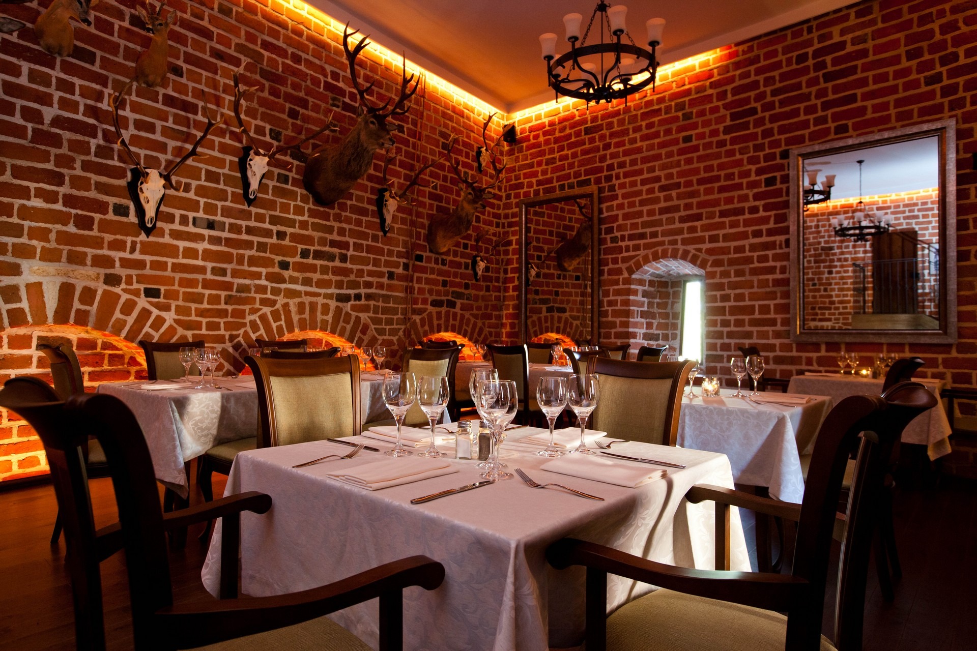 Uroczysta sala restauracyjna z ceglanymi ścianami, dekoracjami myśliwskimi, elegancko nakrytymi stołami i oświetleniem LED.