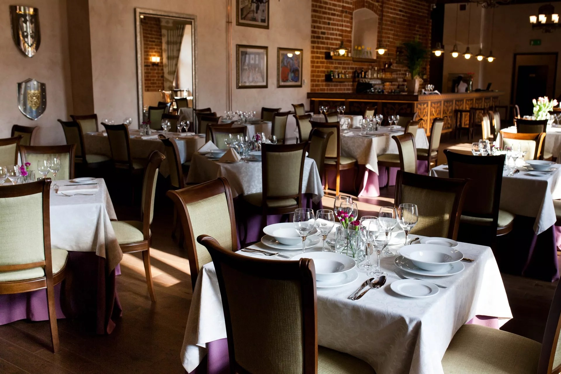 Elegancko nakryte stoły w restauracji z dekoracjami kwiatowymi i elementami wystroju nawiązującymi do średniowiecza, takimi jak tarcze na ścianach.