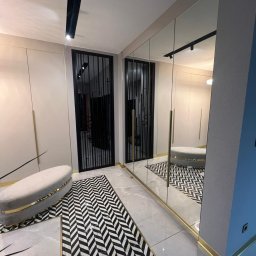 WOODMEBLO Michał Steczko - Nowoczesna szafa wnękowa z lustrzanymi drzwiami i złotymi akcentami w Jasin. Geometryczny wzór dywanu i minimalistyczne oświetlenie podkreślają elegancję wnętrza.