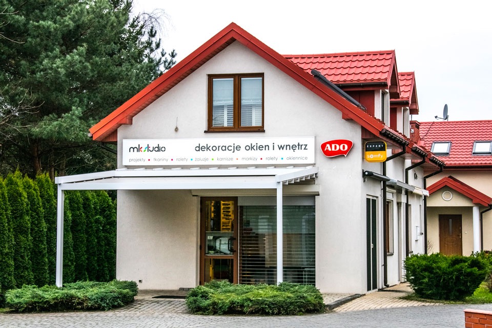 Fasada budynku firmy MK Studio dekoracje okien i wnętrz z ekspozycją produktów za szybą, widoczne reklamy ADO i Somfy Expert.