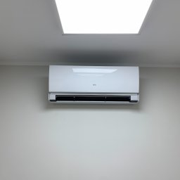 Klimatech Marcin Puc - Nowoczesny, biały klimatyzator Fujitsu zamontowany na jasnoszarej ścianie pod sufitem w minimalistycznym wnętrzu biura lub domu, oświetlony przez kwadratową lampę sufitową.