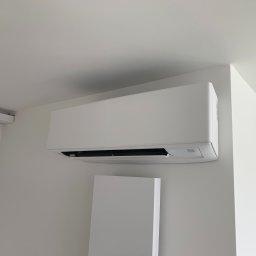 Klimatech Marcin Puc - Biały klimatyzator ścienny zamontowany w minimalistycznym wnętrzu, widoczny fragment drzwi i panel dekoracyjny, oświetlenie sufitowe