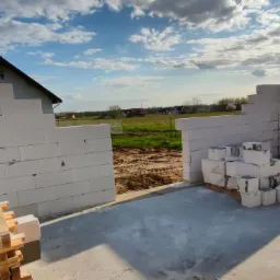 Wznoszone ściany z betonu komórkowego na fundamencie domu jednorodzinnego w otoczeniu zieleni i błękitnego nieba.