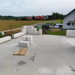 ZBYCHU-Usługi Wielobranżowe Zbigniew Słyż - Wznoszenie ścian z białych bloczków Solbet na fundamencie domu jednorodzinnego, widok na okolicę z polami i zabudowaniami.