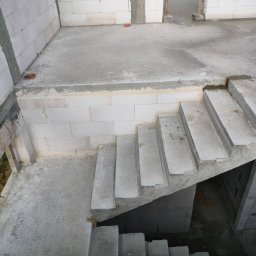 ZBYCHU-Usługi Wielobranżowe Zbigniew Słyż - Surowe schody betonowe wewnątrz budynku w stanie surowym, widoczne ściany z białego betonu komórkowego i surowy betonowy strop, fragment instalacji kanalizacyjnej w podłodze.