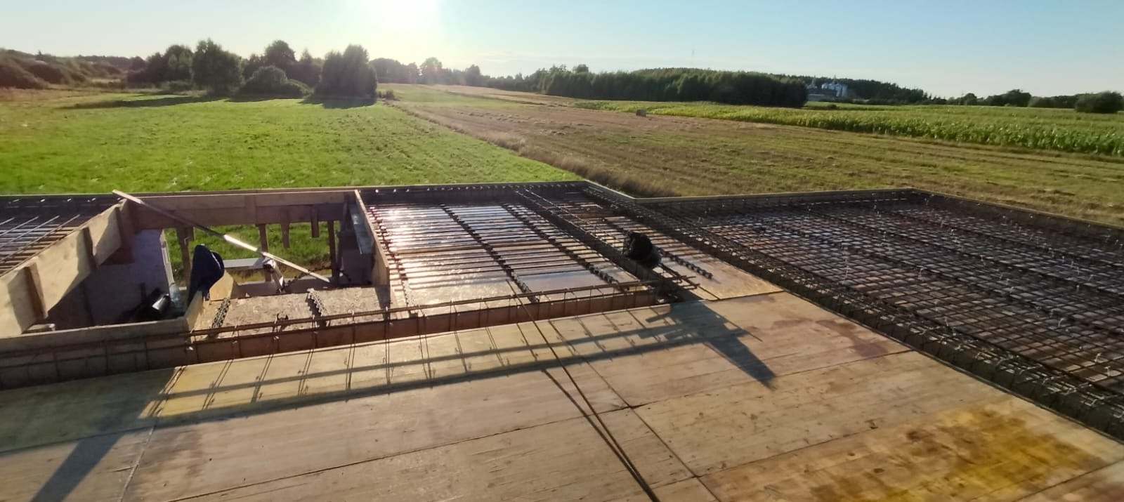 Zbrojenie płyty fundamentowej na drewnianym szalunku, widok z góry na tle zielonego krajobrazu.