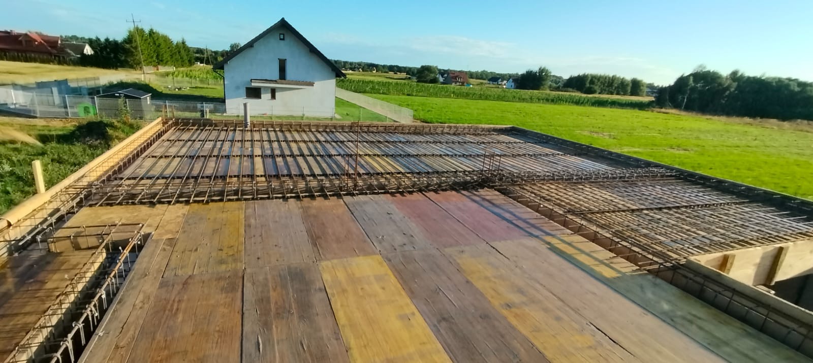 Zbrojenie stropu na deskowaniu z widokiem na budynek w tle, ujęcie z góry.