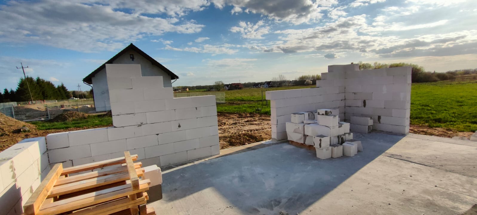 Wznoszone ściany z betonu komórkowego na fundamencie domu jednorodzinnego w otoczeniu zieleni i błękitnego nieba.