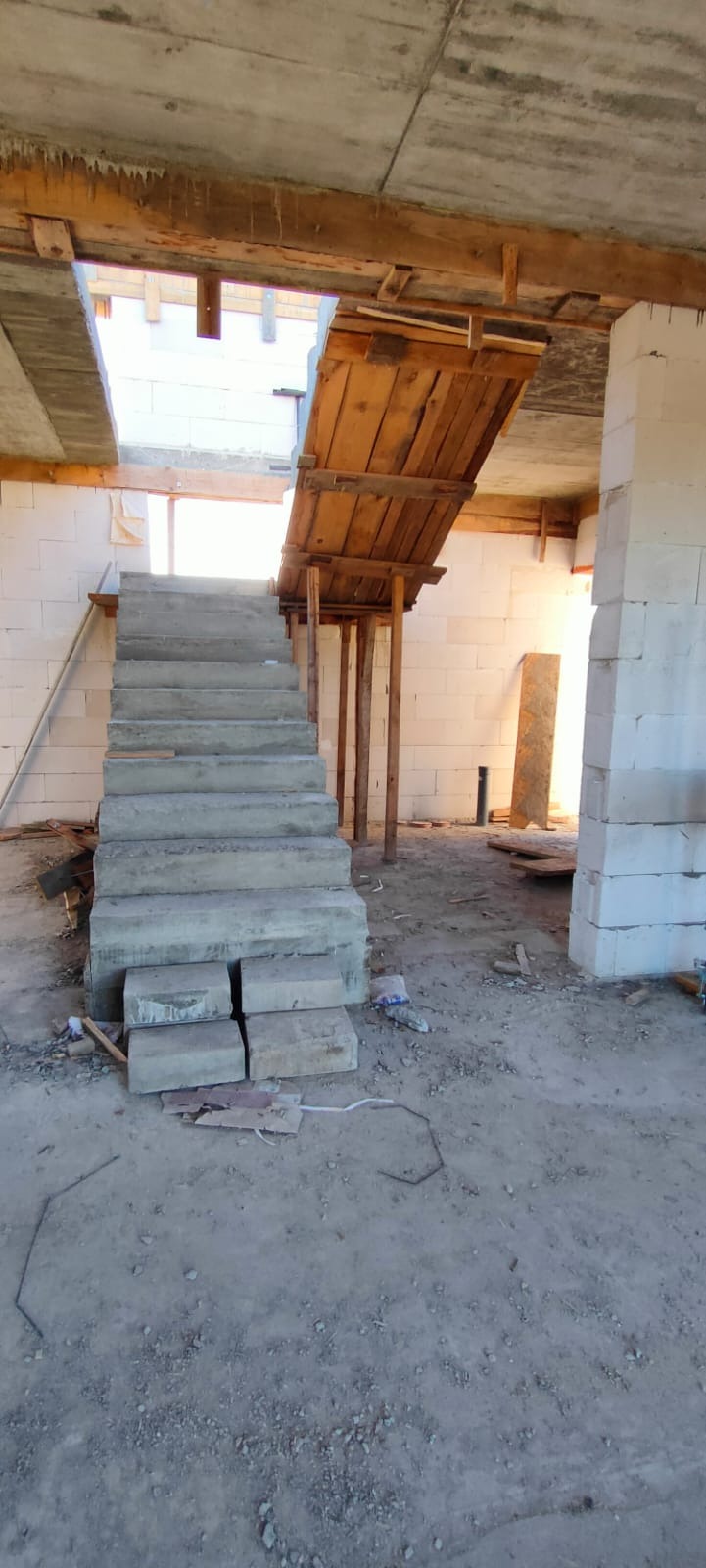 Surowe betonowe schody wewnętrzne w trakcie budowy domu, wsparte drewnianym szalunkiem, ściany z białego bloczka.