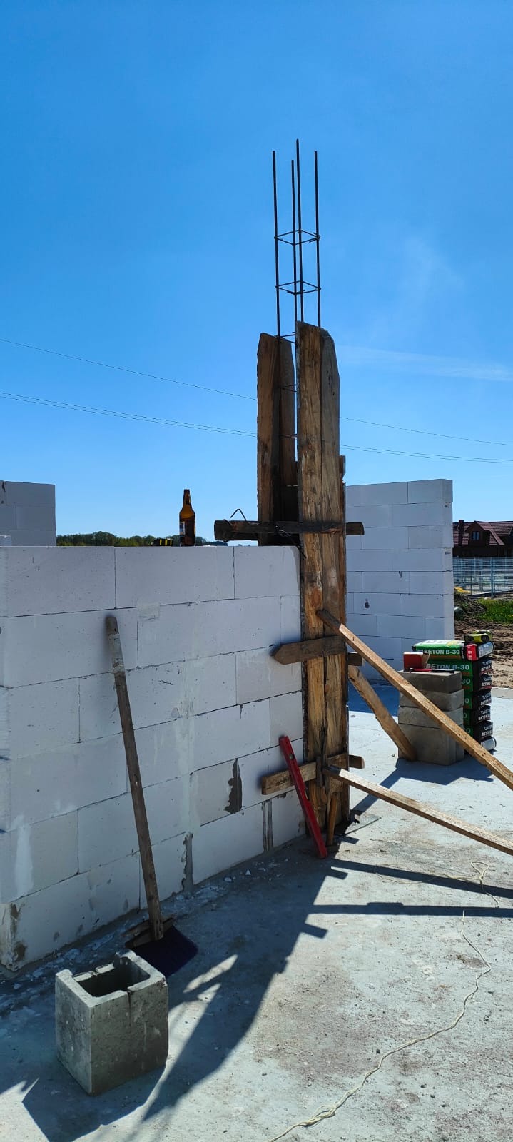 Wznoszenie ściany z betonu komórkowego z drewnianym szalunkiem zbrojonej kolumny, na murze stoi butelka po piwie.