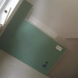 Montaż płyty karton gips na ścianie w trakcie remontu, widoczne otwory na instalacje i profile narożne, surowy stan wykończenia.