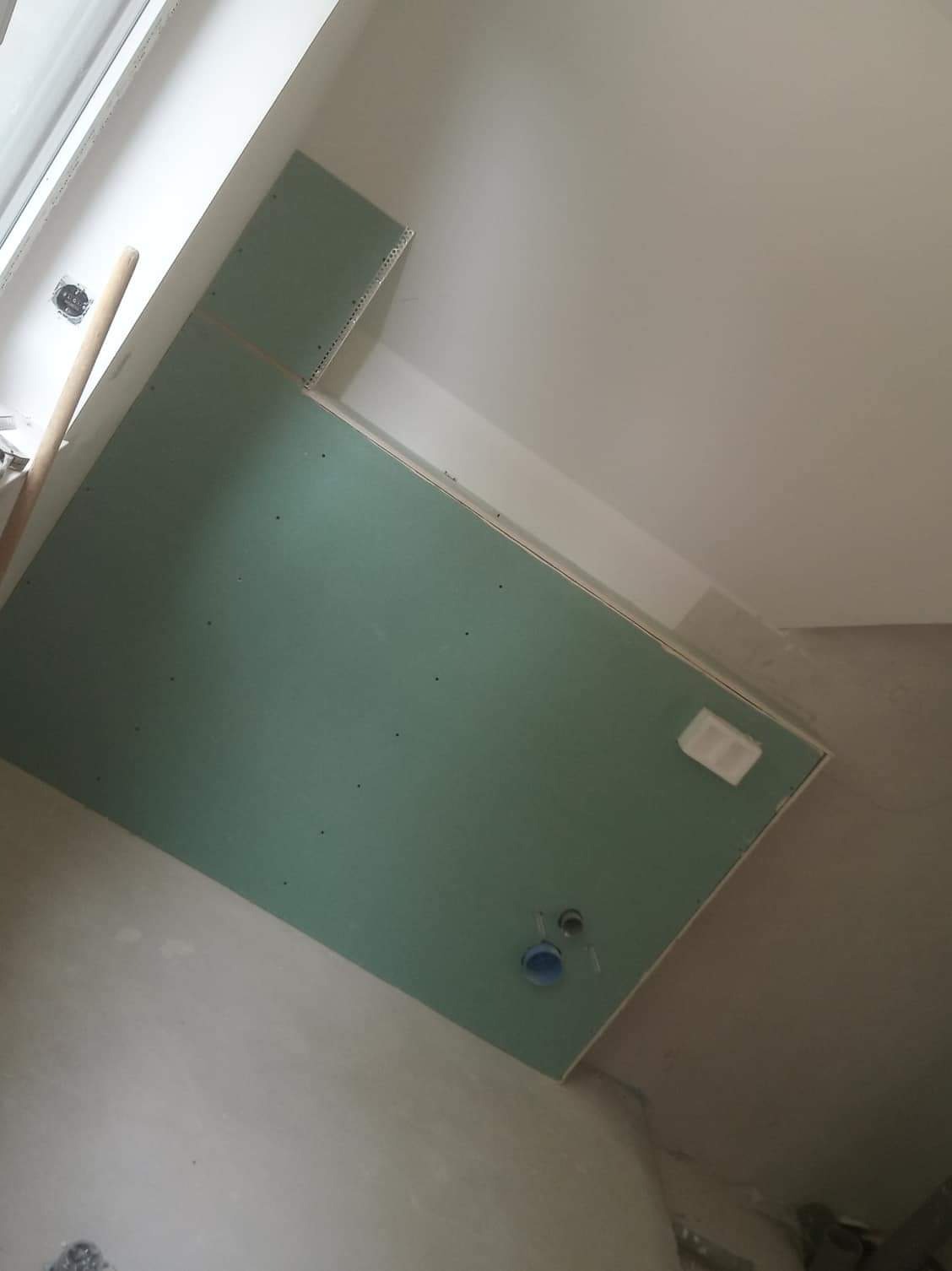 Montaż płyty karton gips na ścianie w trakcie remontu, widoczne otwory na instalacje i profile narożne, surowy stan wykończenia.