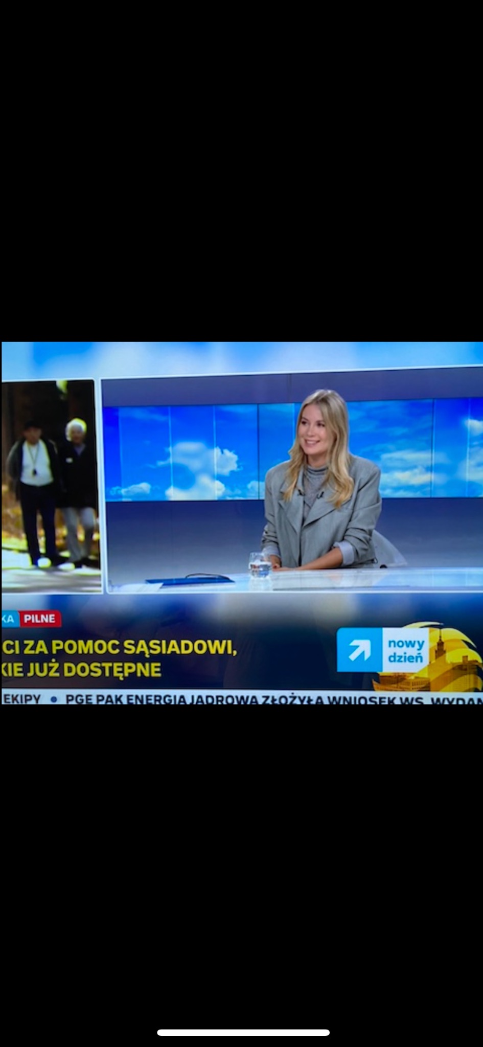 Prezenterka w studiu telewizyjnym, omawia temat pomocy sąsiedzkiej. Na ekranie obok widoczni seniorzy. Logo stacji w prawym dolnym rogu.