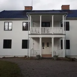 Dwupiętrowy dom z białymi ścianami i ciemnymi oknami po malowaniu elewacji, widoczny fragment rusztowania po lewej stronie.