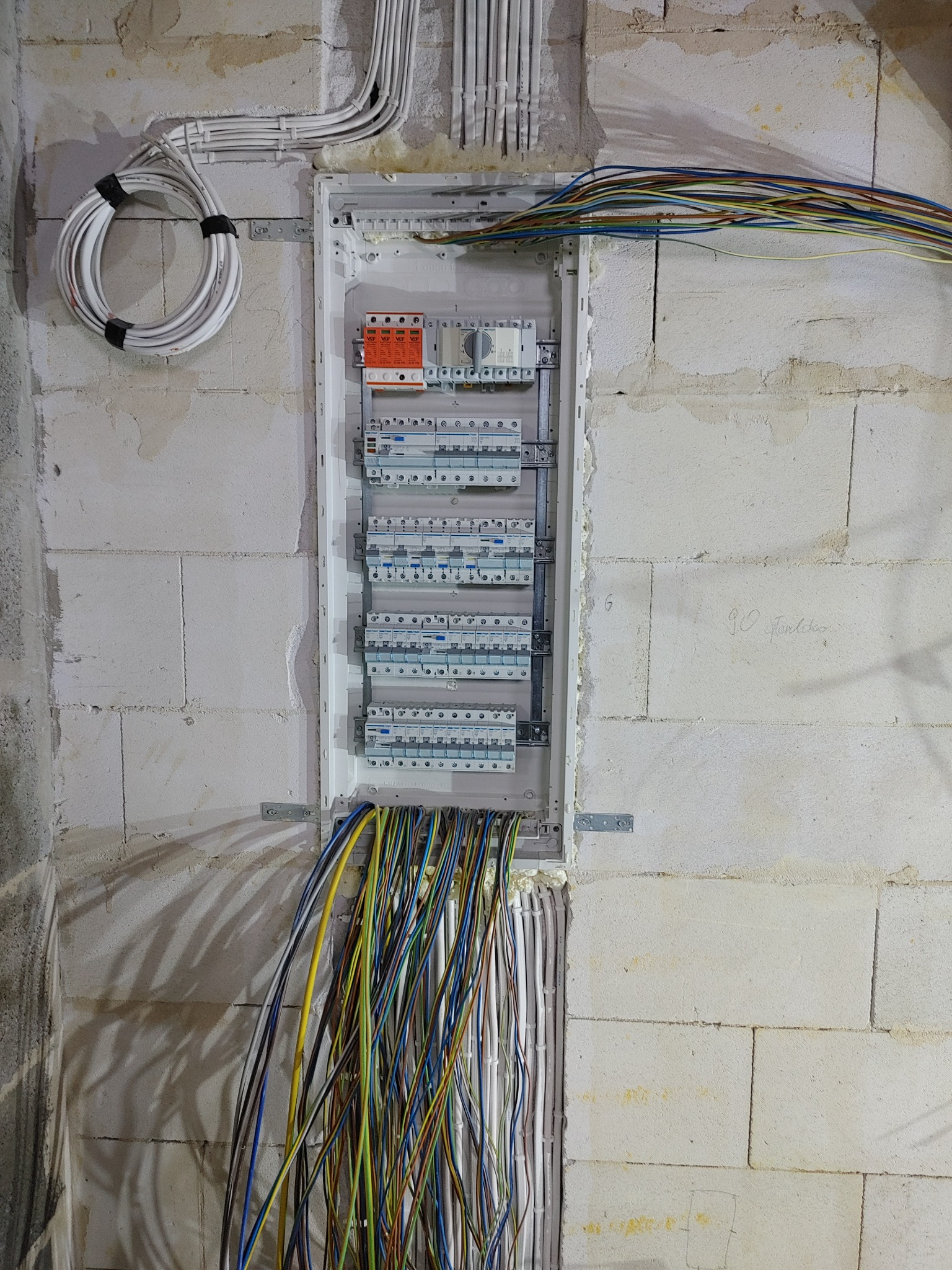 Rozdzielnica elektryczna w stanie montażu w surowym wnętrzu, widoczne liczne przewody i zabezpieczenia, ściany z betonu komórkowego z widocznymi śladami budowy.