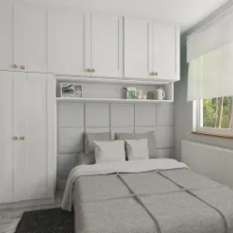 Nowoczesna sypialnia z zabudową meblową w kolorze białym, obejmującą szafy wiszące i stojące, zintegrowane z tapicerowanym wezgłowiem łóżka i półką z dekoracjami, oświetlona naturalnym światłem...