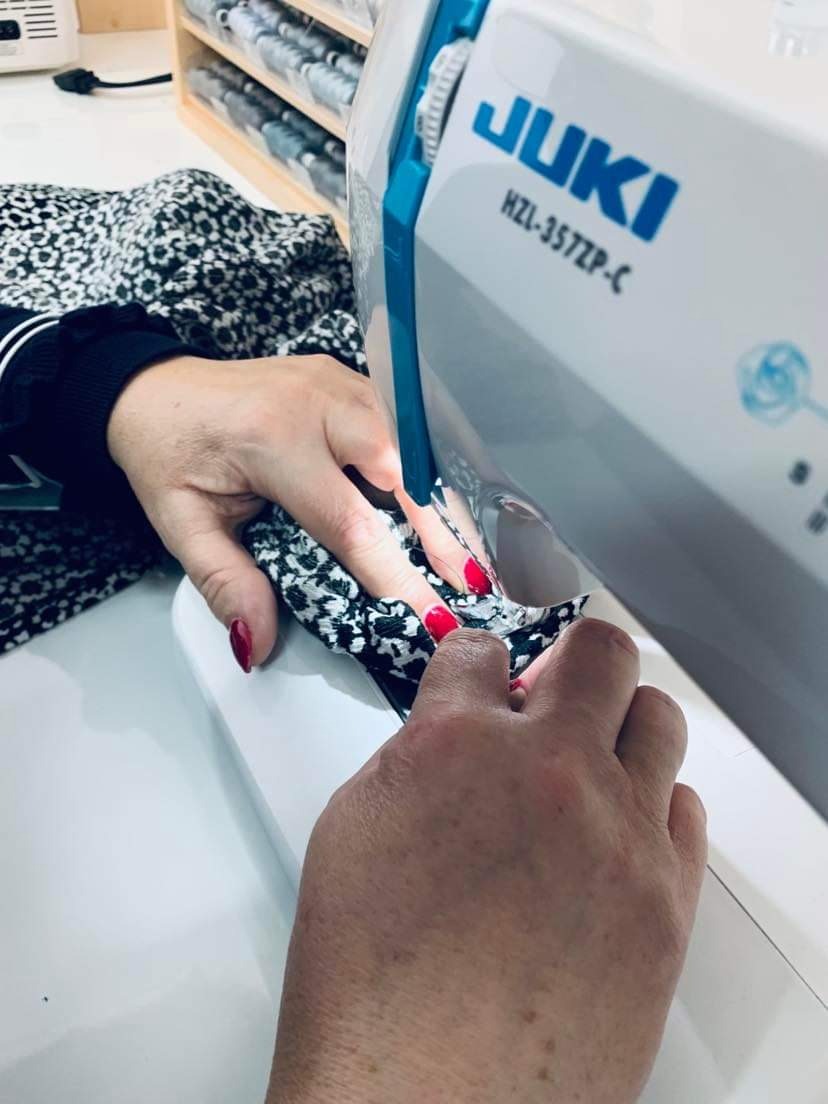 Kobieta szyje wzorzysty materiał na białej maszynie do szycia JUKI HZL-357ZP-C, z czerwonym manicure.