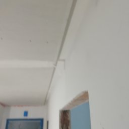 Dami.CON.Truct. - Wnętrze w trakcie prac wykończeniowych: widoczny sufit podwieszany, ściany przygotowane do malowania, fragment otworu drzwiowego bez ościeżnicy.