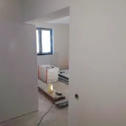 Wnętrze w trakcie remontu, widoczne płyty izolacyjne, narzędzia i przygotowane ściany z widocznym otworem na gniazdko elektryczne.