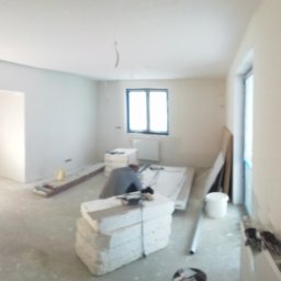 Dami.CON.Truct. - Wnętrze w trakcie prac wykończeniowych: widoczne płyty do montażu, narzędzia i pracownik przy pracy, surowe ściany i podłoga, przygotowanie do montażu instalacji.