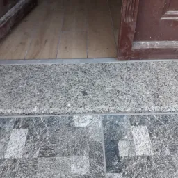 Szare płytki podłogowe ułożone na posadzce, graniczące z progami drzwi z jasnego drewna i szarego kamienia.