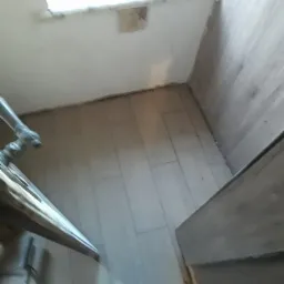 Ułożone płytki podłogowe w małej łazience z fragmentem umywalki i widocznym oknem w tle, w trakcie remontu.