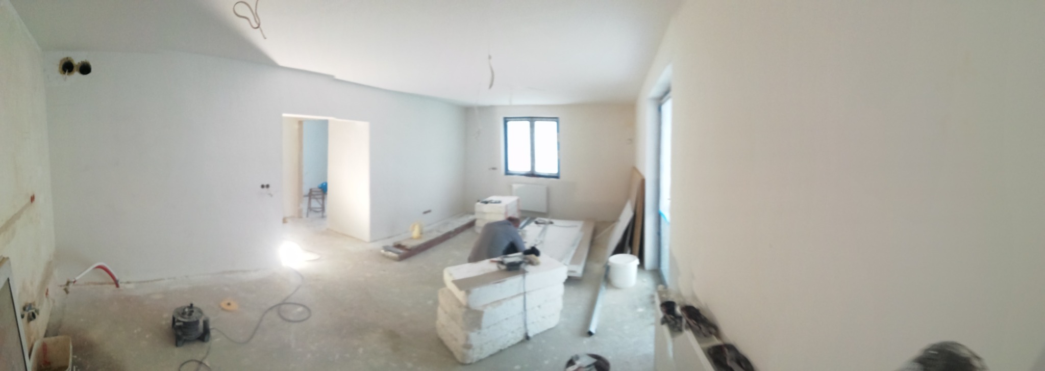 Wnętrze w trakcie prac wykończeniowych: widoczne płyty do montażu, narzędzia i pracownik przy pracy, surowe ściany i podłoga, przygotowanie do montażu instalacji.