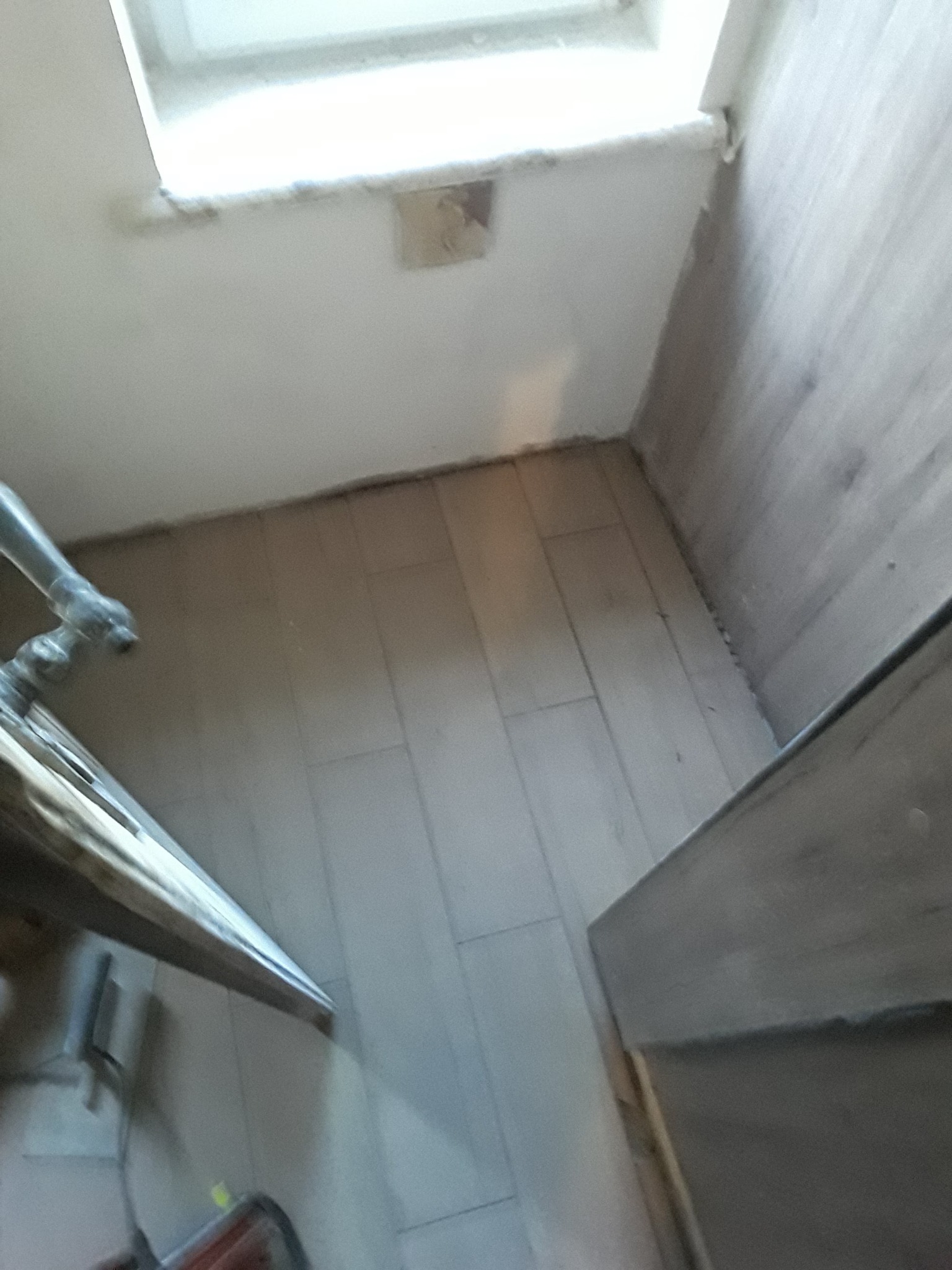 Ułożone płytki podłogowe w małej łazience z fragmentem umywalki i widocznym oknem w tle, w trakcie remontu.