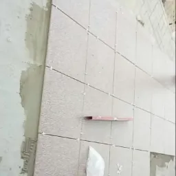 Układanie płytek elewacyjnych z użyciem krzyżyków dystansowych, widoczny fragment ściany z nałożonym klejem i poziomica.