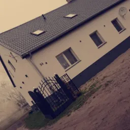 Dwukondygnacyjny dom z białymi ścianami, ciemną podmurówką i grafitowym dachem z lukarnami, widziany pod kątem, z numerem domu '54' i metalową bramką.