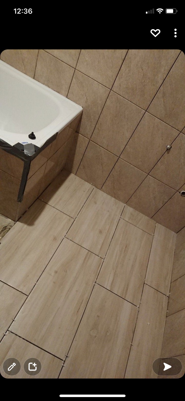 Układanie beżowych płytek podłogowych w łazience, widoczna wanna zabezpieczona taśmą, krzyżyki dystansowe między płytkami.