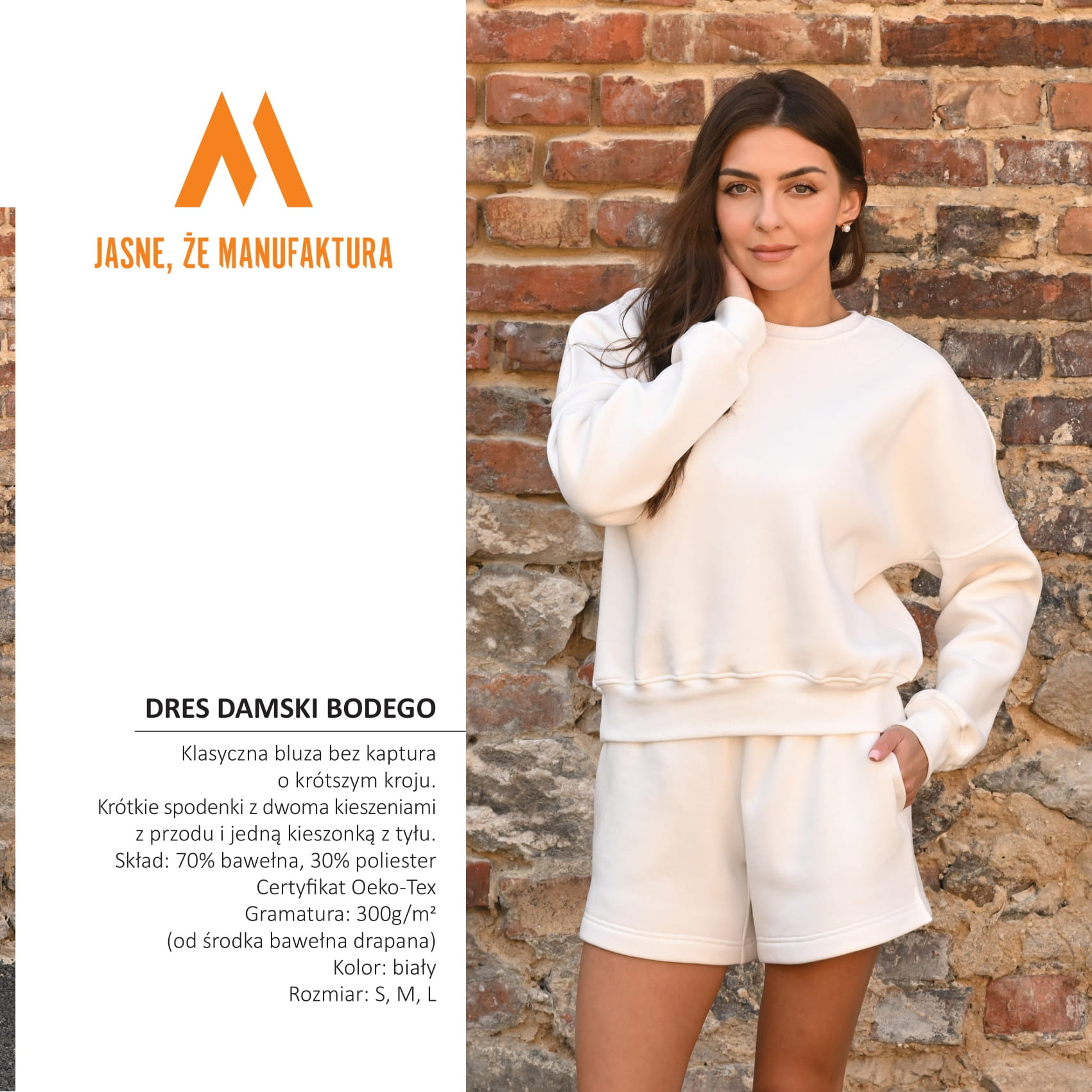 Kobieta prezentuje biały dres damski (bluza i spodenki) na tle ceglanej ściany. Widoczne detale kroju i materiału. Komfortowy styl.