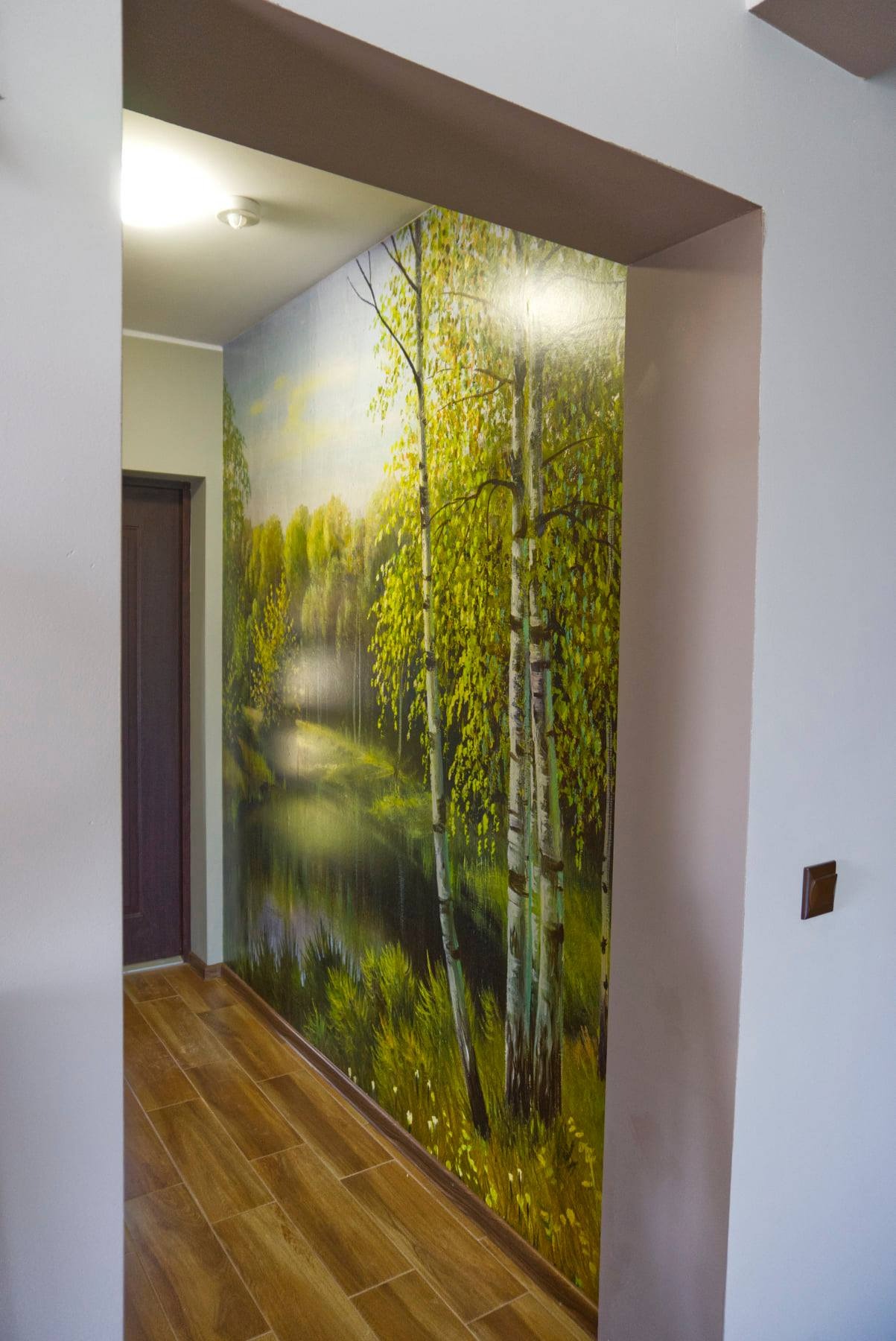 Fotorealistyczna tapeta z motywem brzozowego lasu nad brzegiem jeziora, zamontowana na ścianie w korytarzu z drewnianą podłogą, widok z perspektywy wejścia do pomieszczenia.