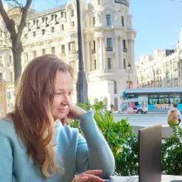 Kobieta z laptopem Yoga w kawiarni na tle architektury Madrytu, być może podczas lekcji online. W tle budynek Metropolis i autobus turystyczny.